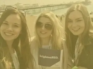 Hannah, Caroline, and Alex at Brighton beach on Brighton SEO day with yellow image overlay