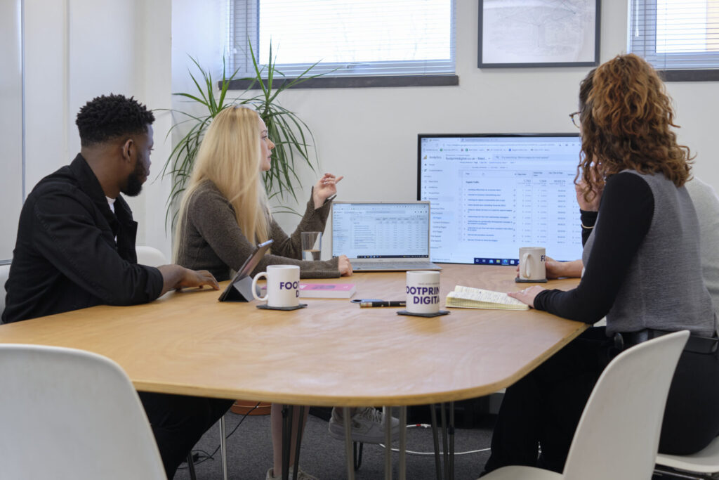 Full colour office shot team photo in meeting room one emeke, charlotte, bailey
