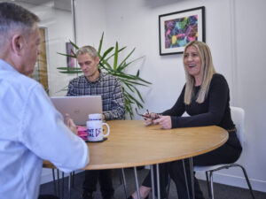 Dave, Sarah, and Jon in meeting room 2 at the office in a meeting full colour